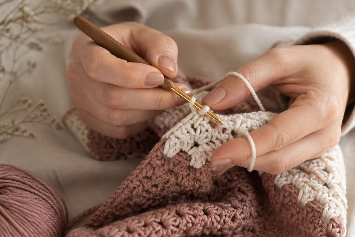 Mains qui travaillent une pièce au crochet dans des tons rose et crème