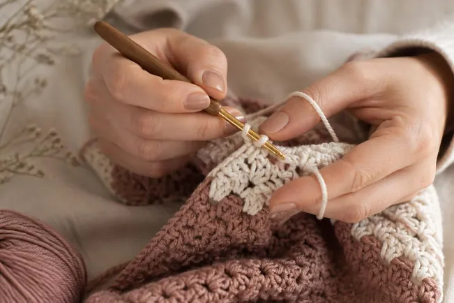 Mains qui travaillent une pièce au crochet dans des tons rose et crème